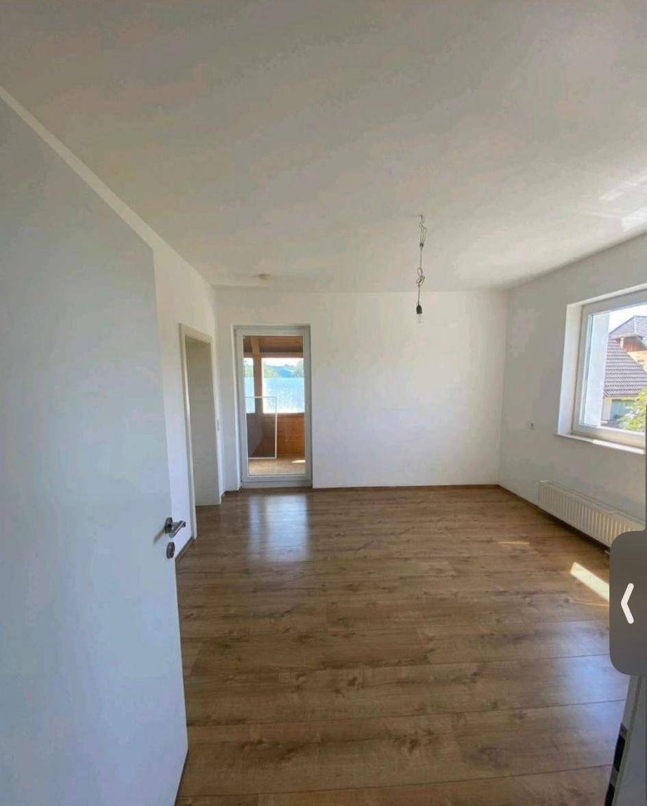 Geräumiges Zimmer mit Laminatboden, weißen Wänden und Zugang zu einem Balkon.