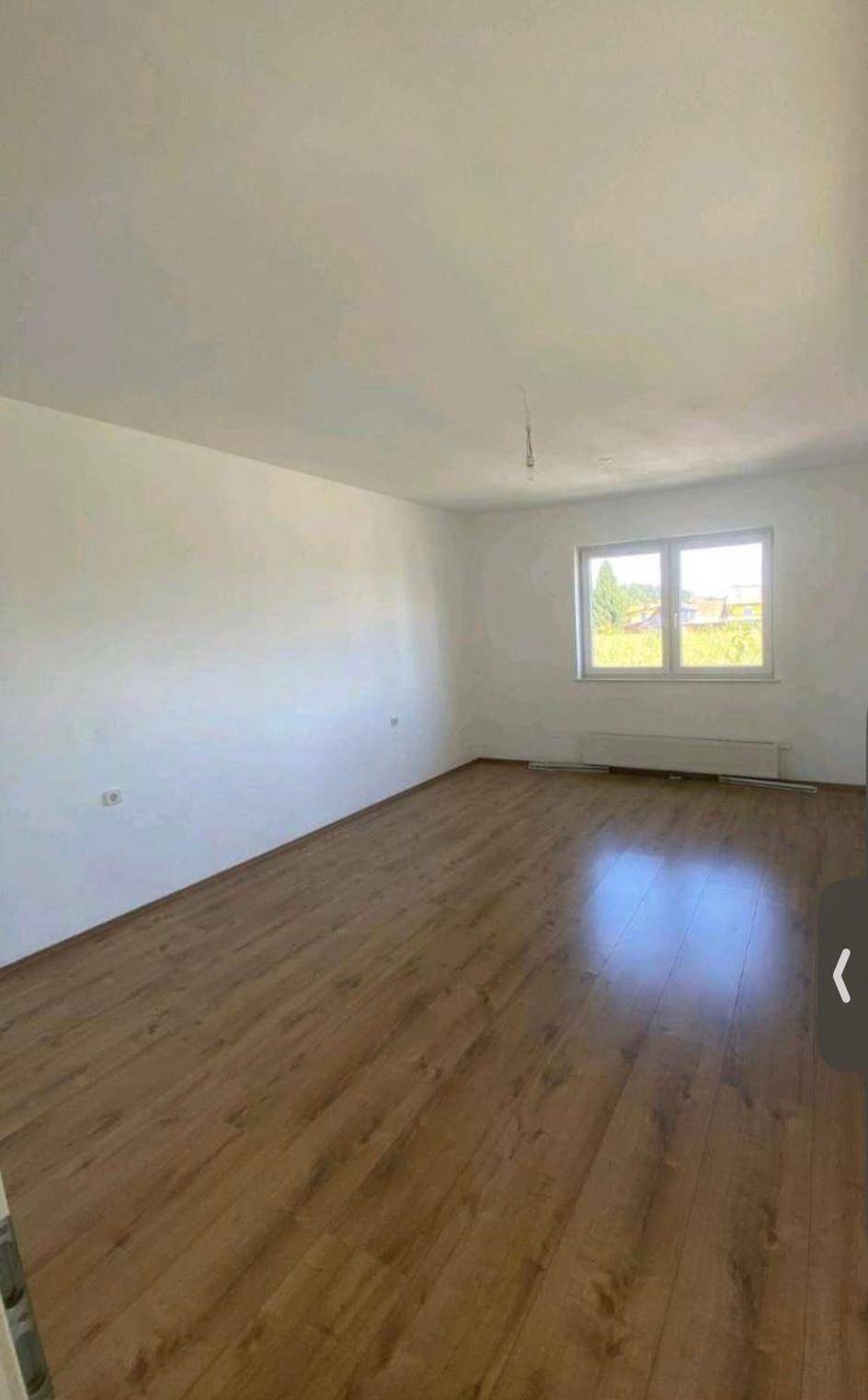 Ruhiges Zimmer mit Laminatboden, weißen Wänden und Fenster mit Blick ins Freie.