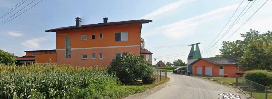 Ansicht eines orangefarbenen Gebäudes von der Straße, umgeben von grünen Feldern.