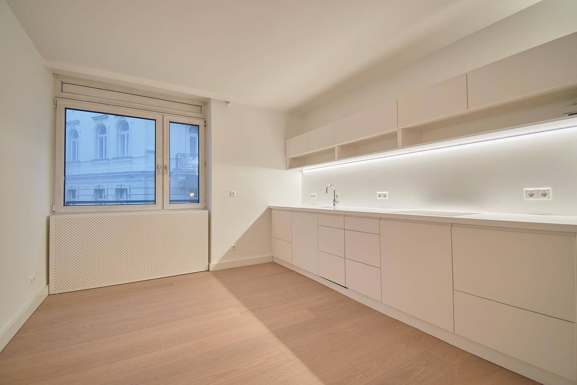 Offener Wohnbereich mit moderner Küchenzeile, großem Fenster und hellem Holzboden.