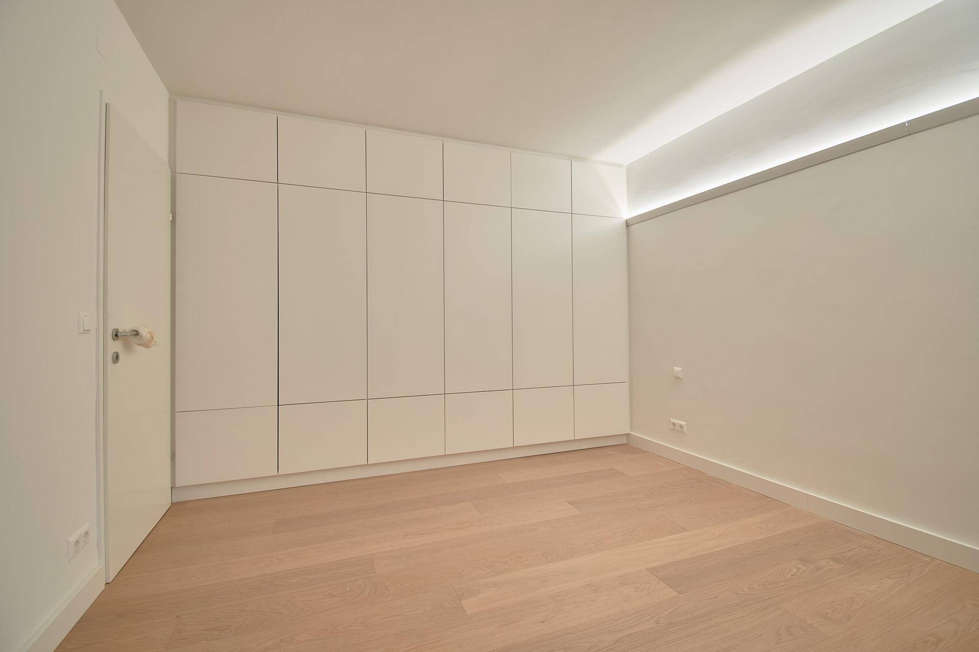 Moderner Raum mit integrierten weißen Schränken und hellem Holzboden, minimalistisches Design.