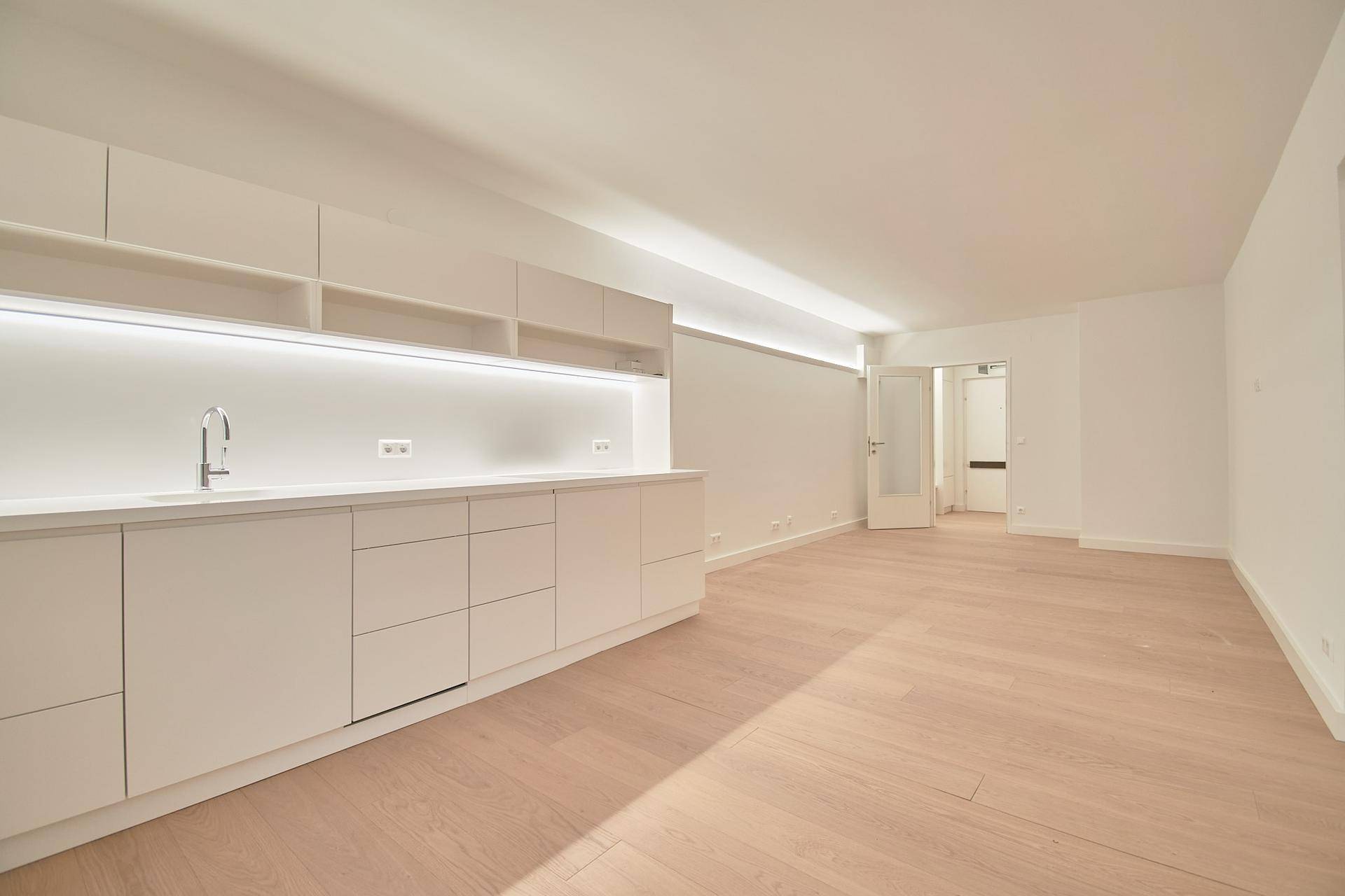 Heller Raum mit moderner Küchenzeile und Holzboden, Blick auf eine Innentür.