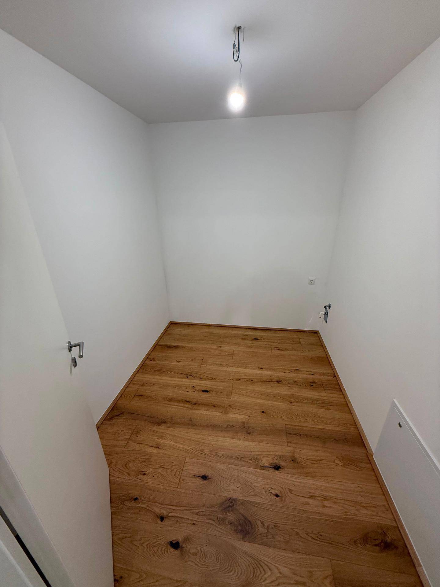 Kleiner, leerer Raum mit Holzboden, ideal als Abstellraum oder begehbarer Kleiderschrank nutzbar.