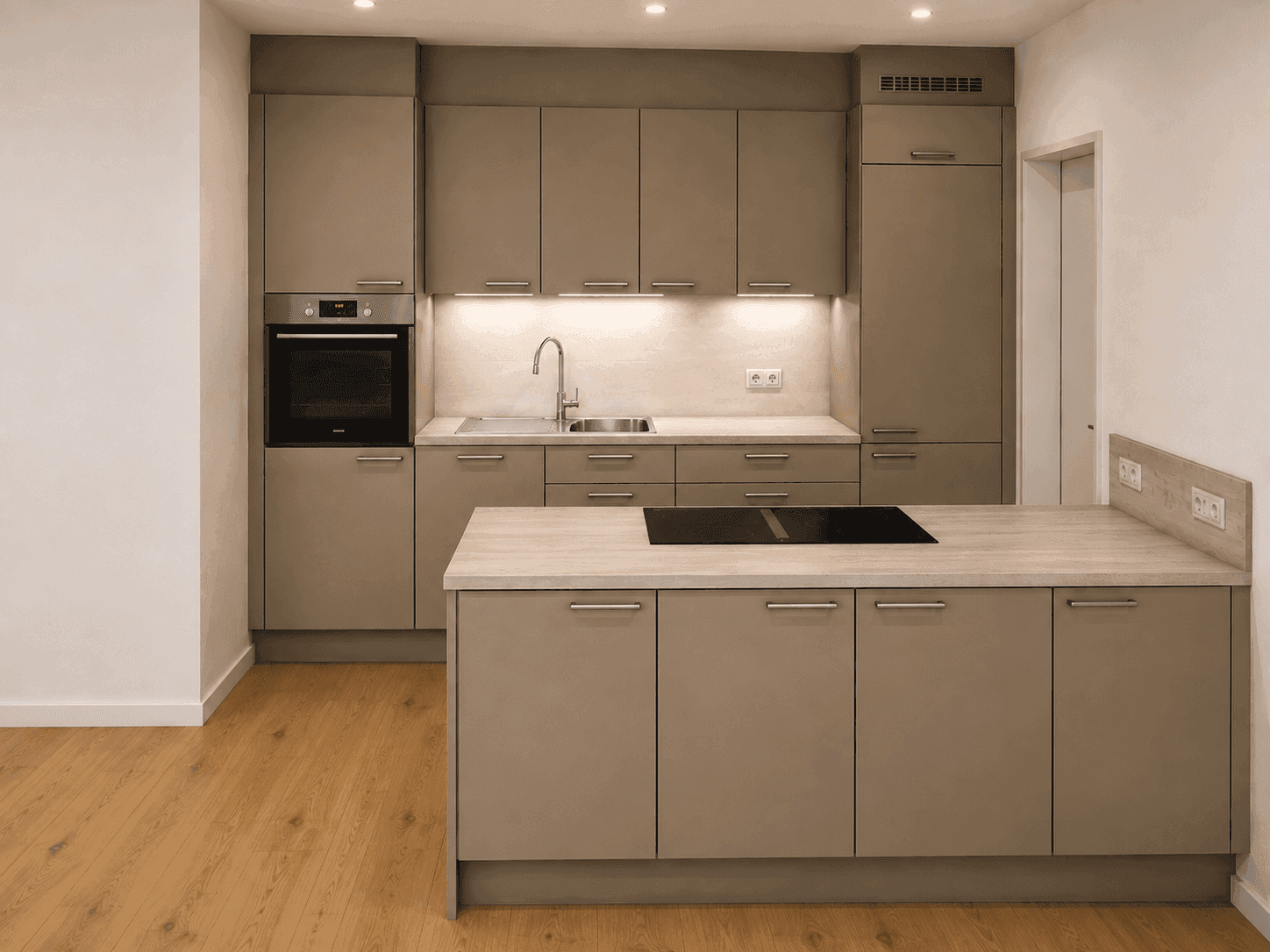 Moderne Einbauküche in Grau mit Kochinsel, integrierten Geräten und hellem Holzboden.