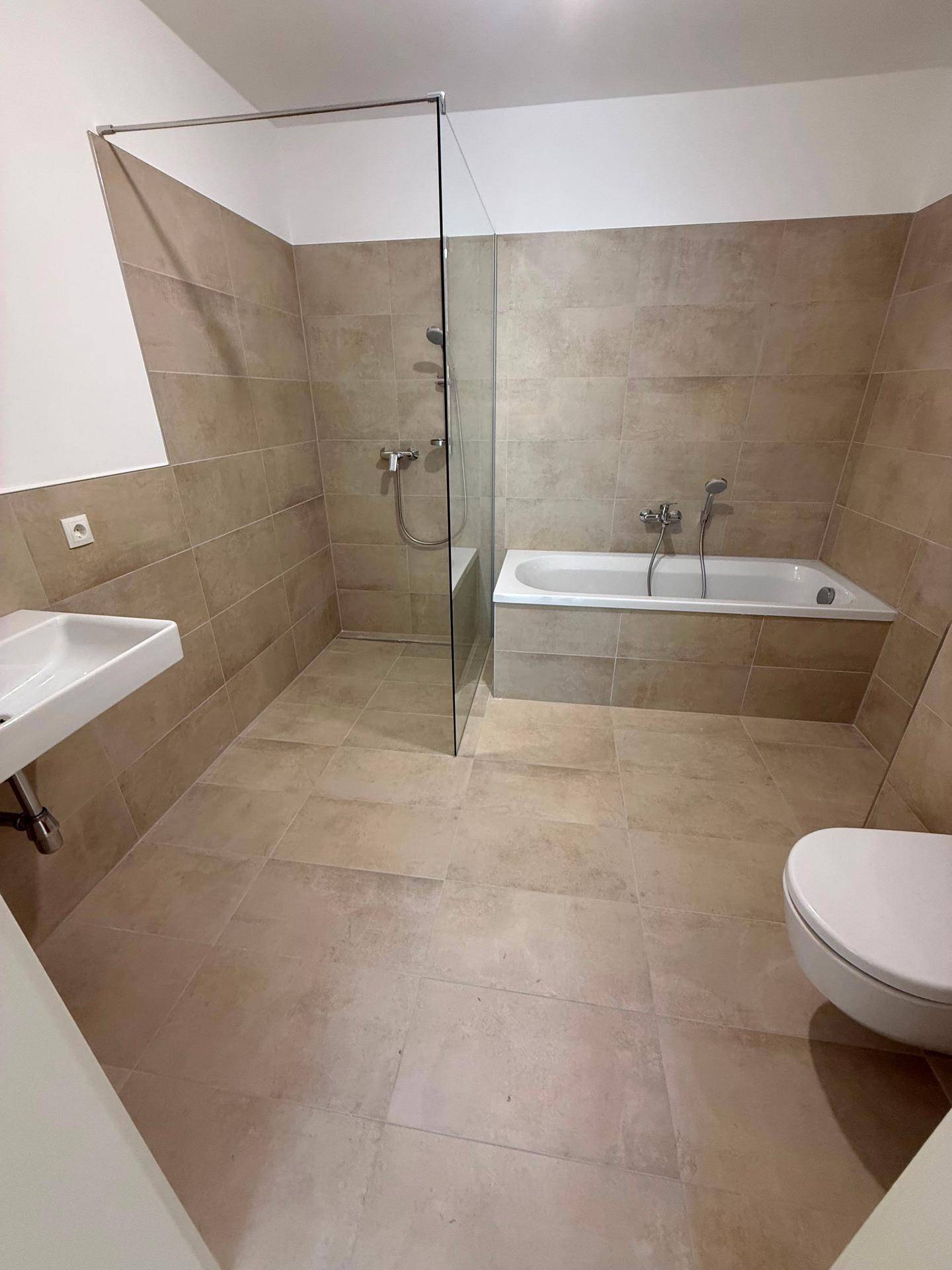 Modernes Badezimmer mit Badewanne, Dusche, Waschbecken und beigefarbenen Fliesen an Wänden und Boden.