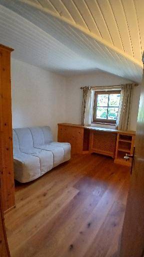 Heller Raum mit Holzboden, gemütlichem Sofa und Holzmöbeln unter einer Holzdecke.