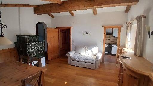 Heller Wohnbereich mit traditionellem Kachelofen, Holzboden und gemütlichem Sofa.