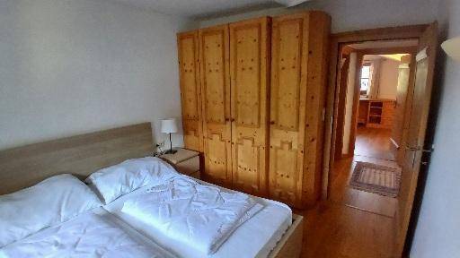 Schlafzimmer mit großem Holzschrank, zwei Betten und Zugang zu einem weiteren Raum.