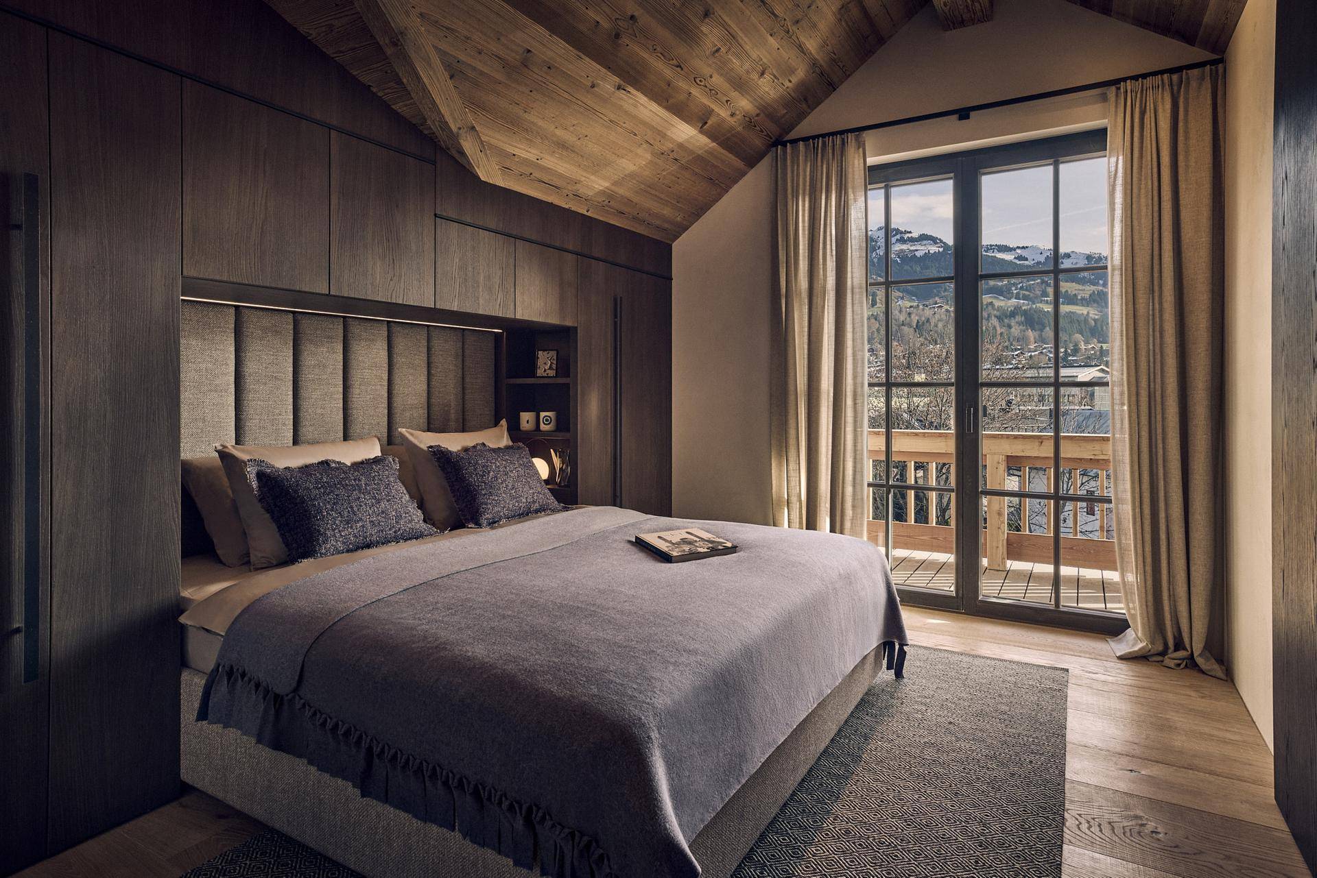 Elegantes Schlafzimmer mit Holzwänden, gepolstertem Kopfteil und Balkonzugang mit Bergblick.