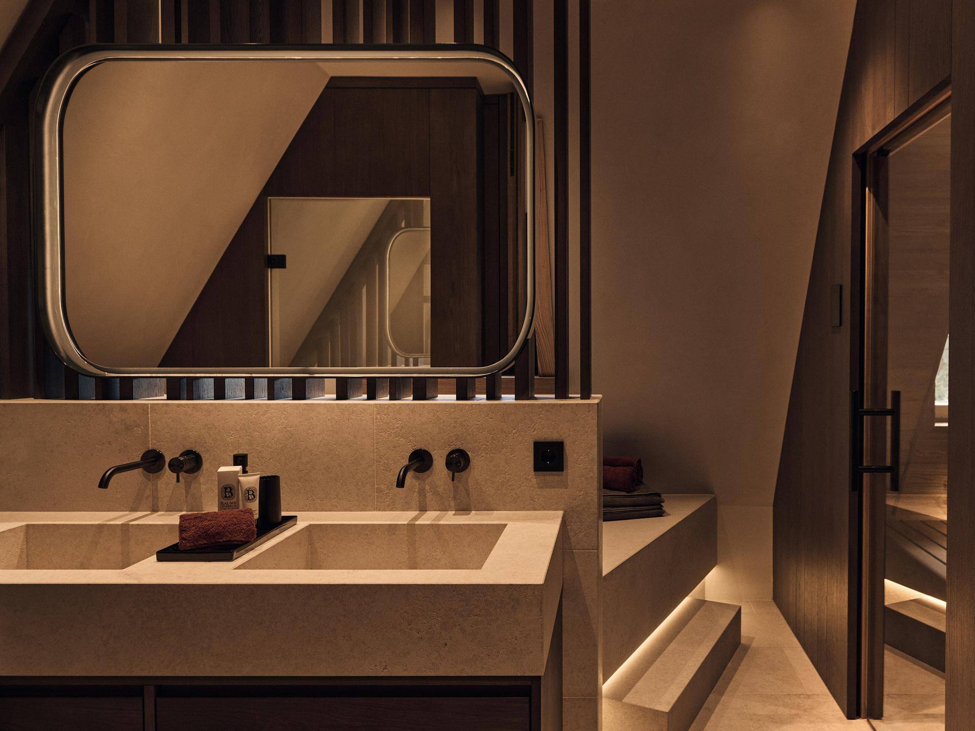 Elegantes Badezimmer mit Doppelwaschbecken, indirekter Beleuchtung und Zugang zur Sauna.