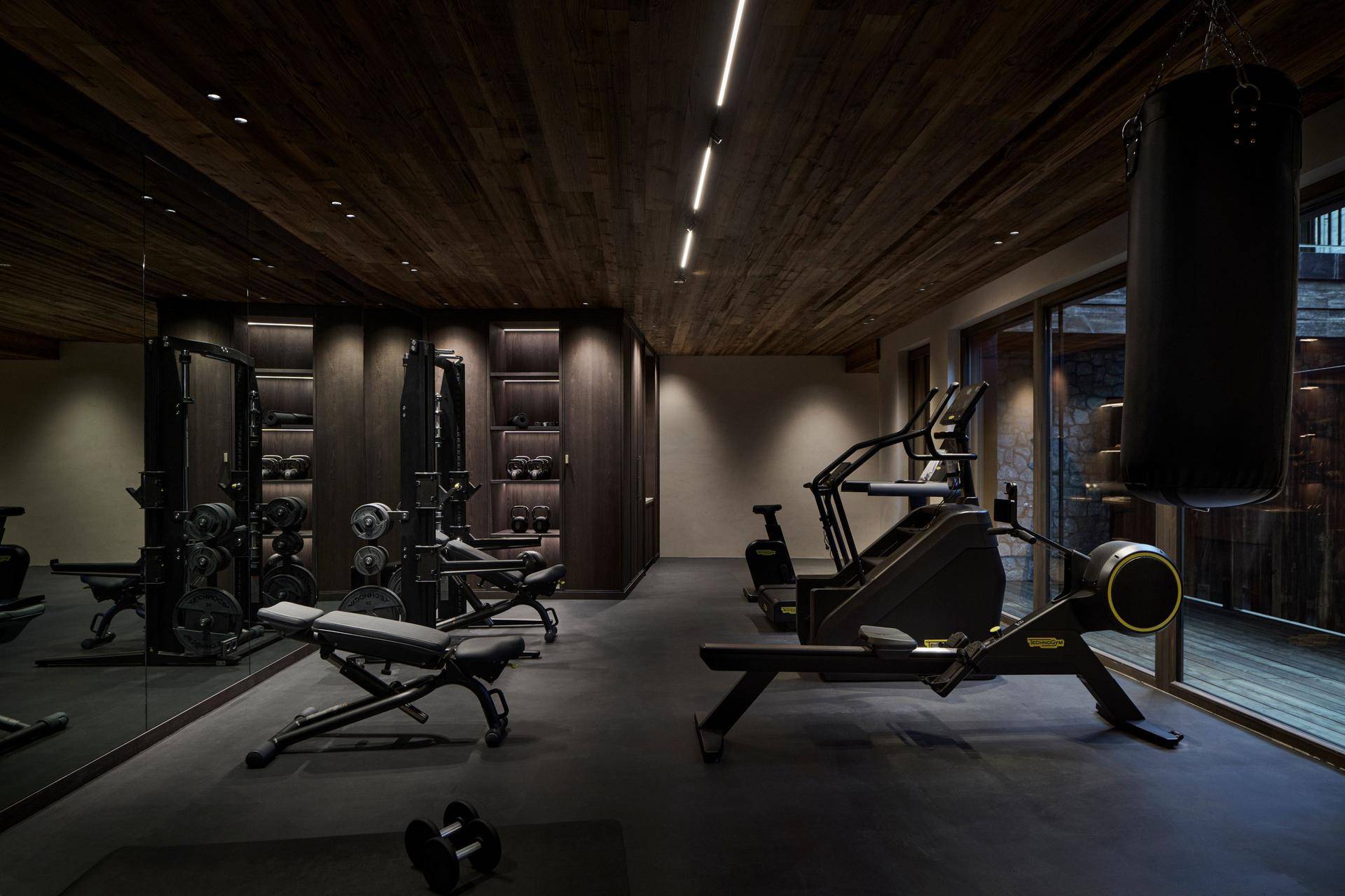 Gut ausgestatteter Fitnessraum mit verschiedenen Trainingsgeräten und dunkler Holzdecke.