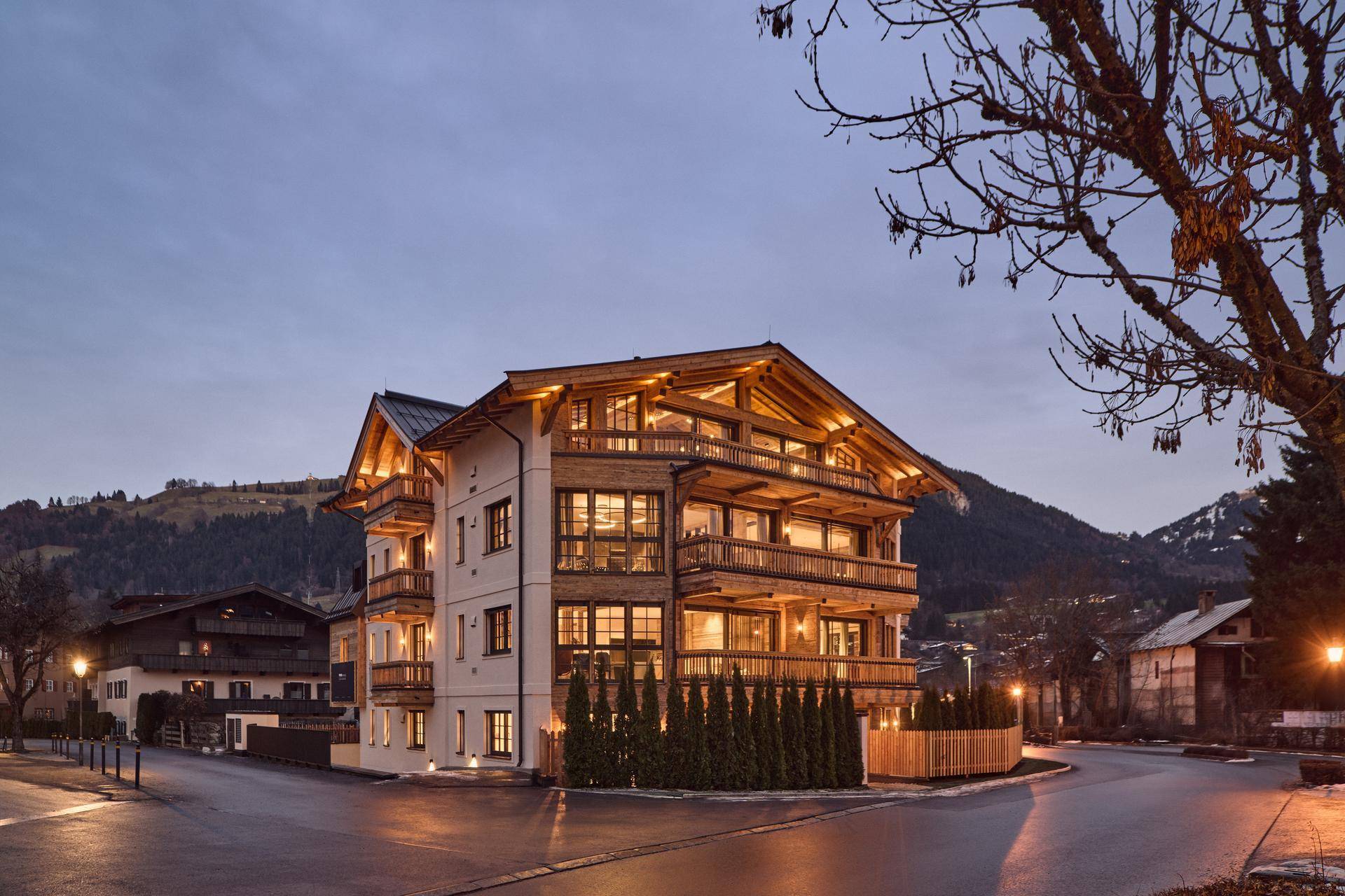 Attraktives Mehrfamilienhaus im alpinen Stil mit Holzfassade und Balkonen bei Abenddämmerung.