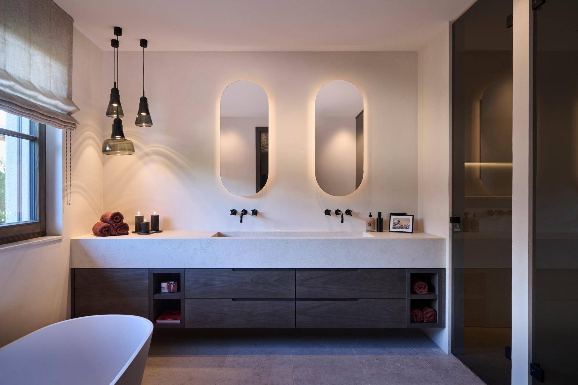 Modernes Badezimmer mit Doppelwaschbecken, beleuchteten Spiegeln, Badewanne und separater Dusche.