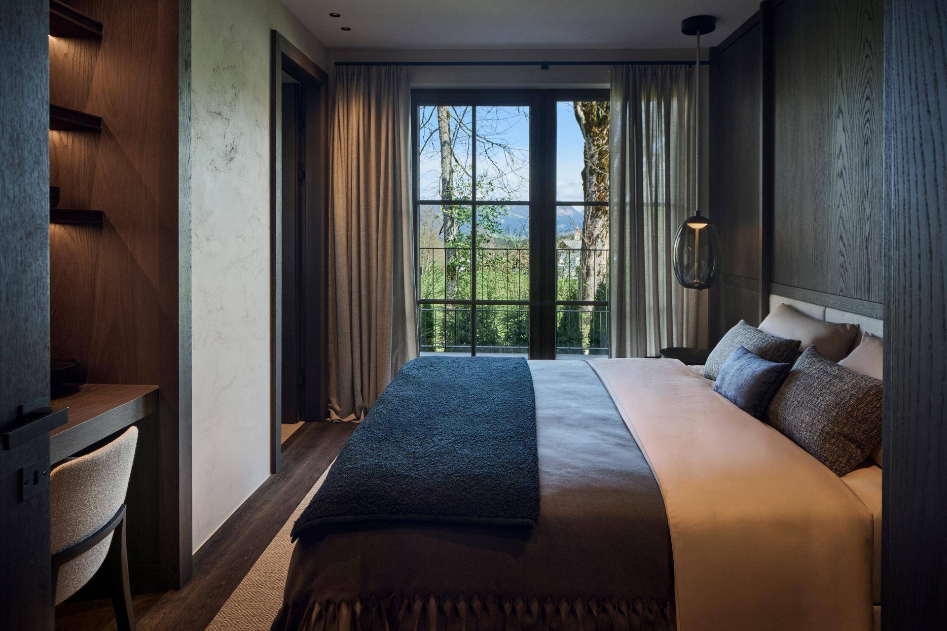 Gemütliches Schlafzimmer mit Schreibtischbereich und großem Fenster mit Blick ins Grüne.