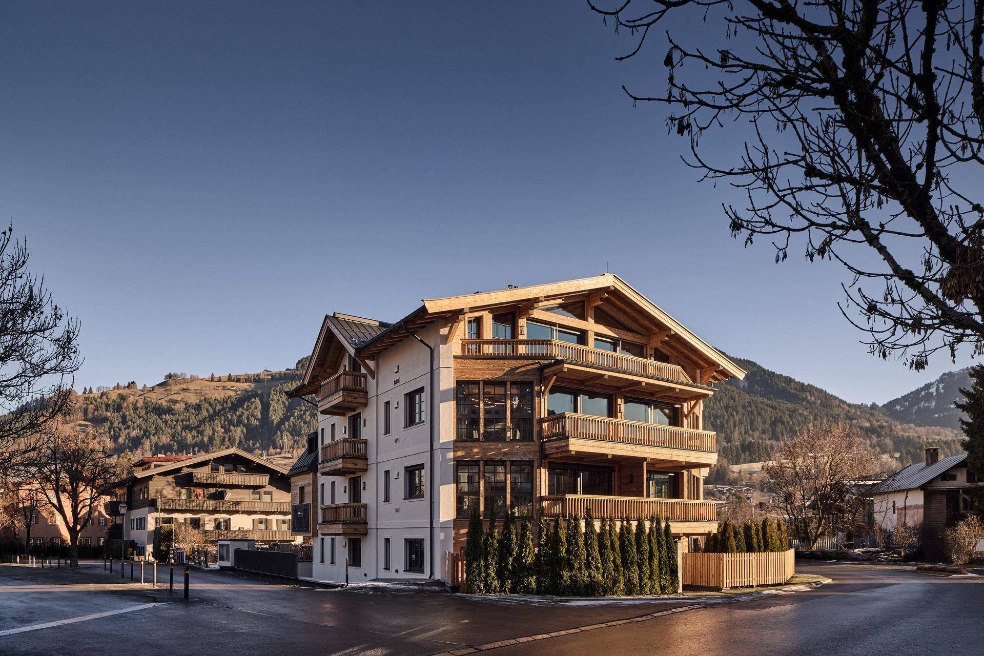 Attraktives Mehrfamilienhaus im alpinen Stil mit Holzfassade und Balkonen in bergiger Umgebung.