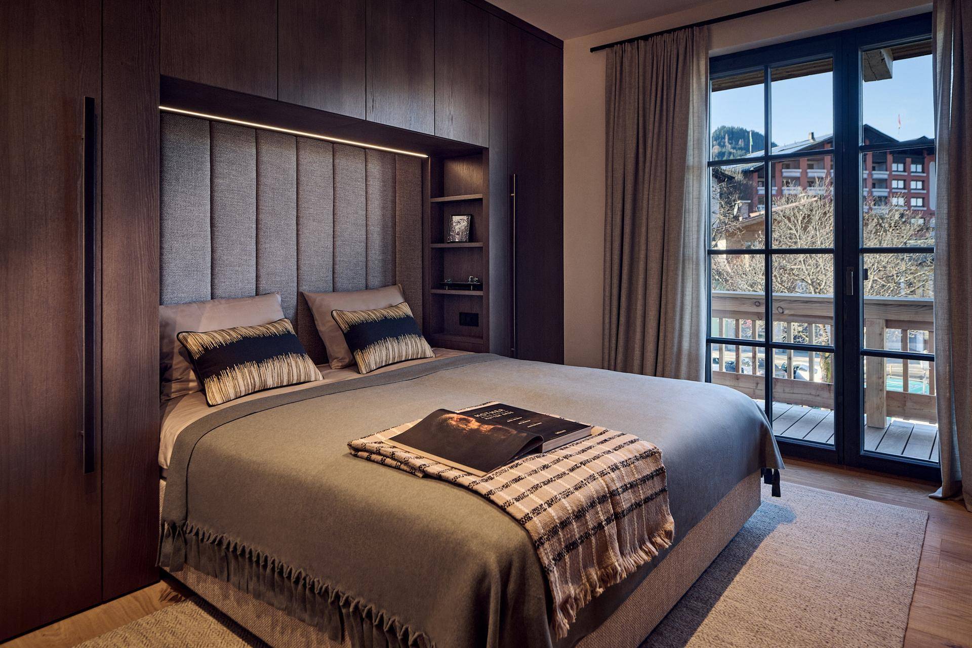 Elegantes Schlafzimmer mit Holzwänden, gepolstertem Kopfteil und Zugang zu einem Balkon mit Bergblick.