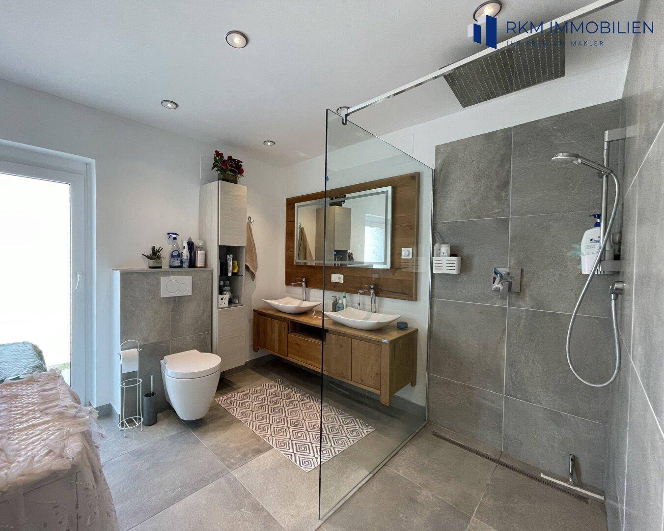 Modernes Badezimmer mit begehbarer Dusche, Doppelwaschbecken und großen grauen Fliesen.
