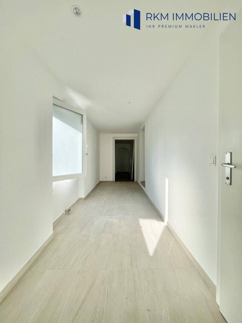 Heller Flur mit modernen Fliesen und viel Tageslicht durch ein großes Fenster.