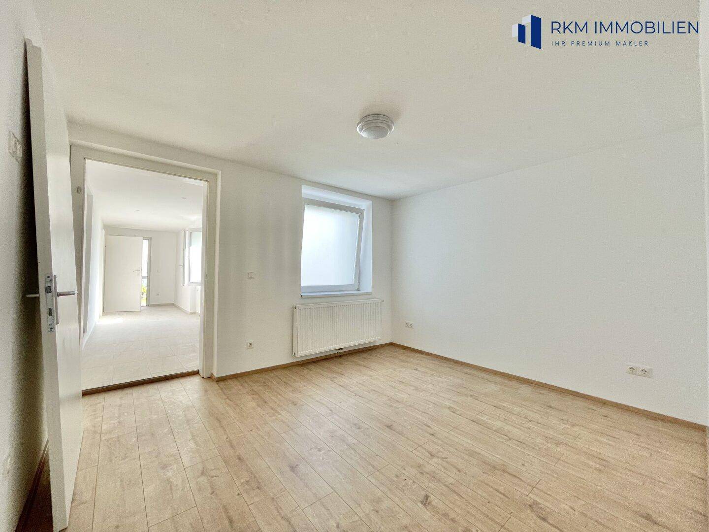 Geräumiges Schlafzimmer mit Holzboden und Blick in einen weiteren hellen Raum.