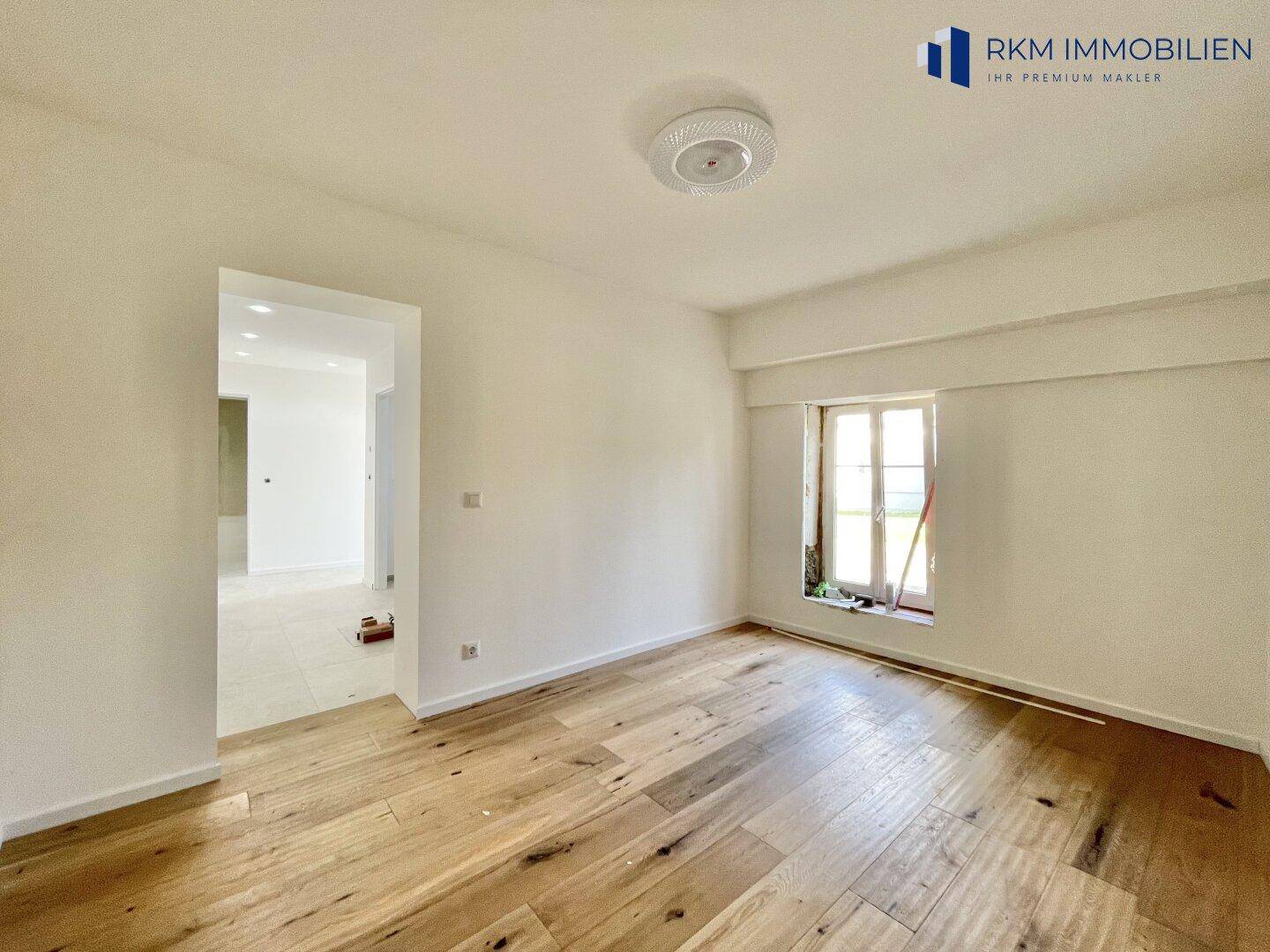 Helles Wohnzimmer mit Holzboden und einem Fenster, das viel Tageslicht hereinlässt.