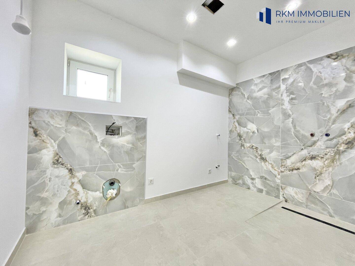 Badezimmer im Bau mit modernen Marmorfliesen und vorbereiteten Anschlüssen.