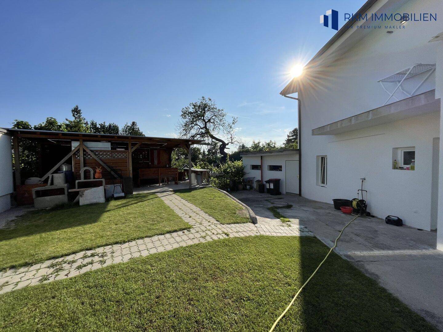Hinterhofbereich mit Rasen, gepflastertem Weg und einem überdachten Sitzbereich.