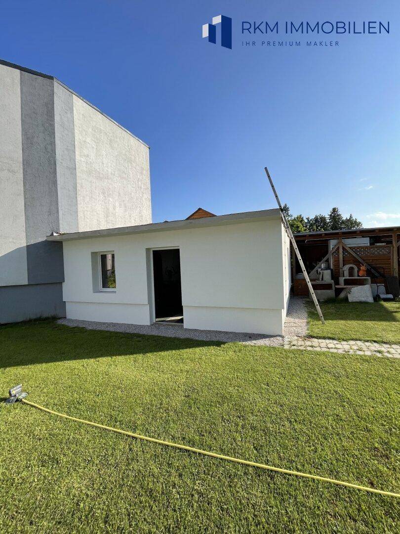 Kleines Nebengebäude im Garten mit weißer Fassade und Fenster.