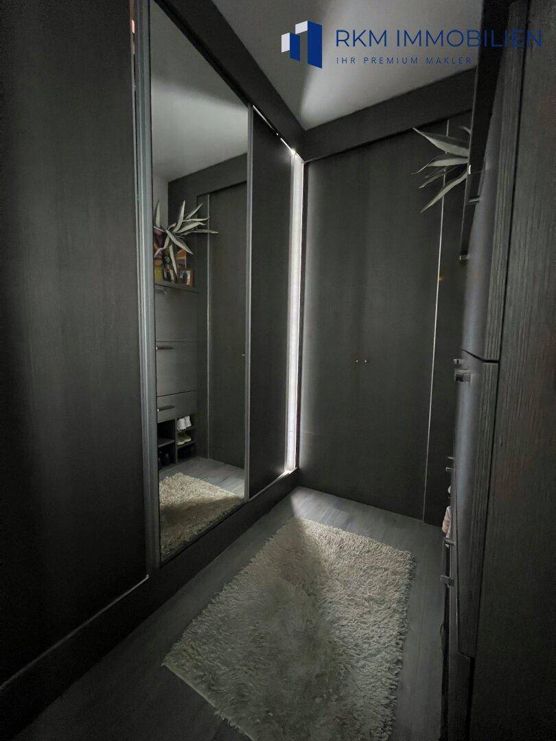 Begehbarer Kleiderschrank mit Spiegeltüren und dunklen Einbauschränken.