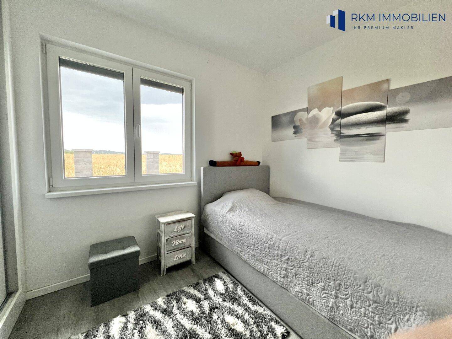 Helles Kinderzimmer mit Einzelbett, kleinem Nachttisch und Blick auf die Landschaft.