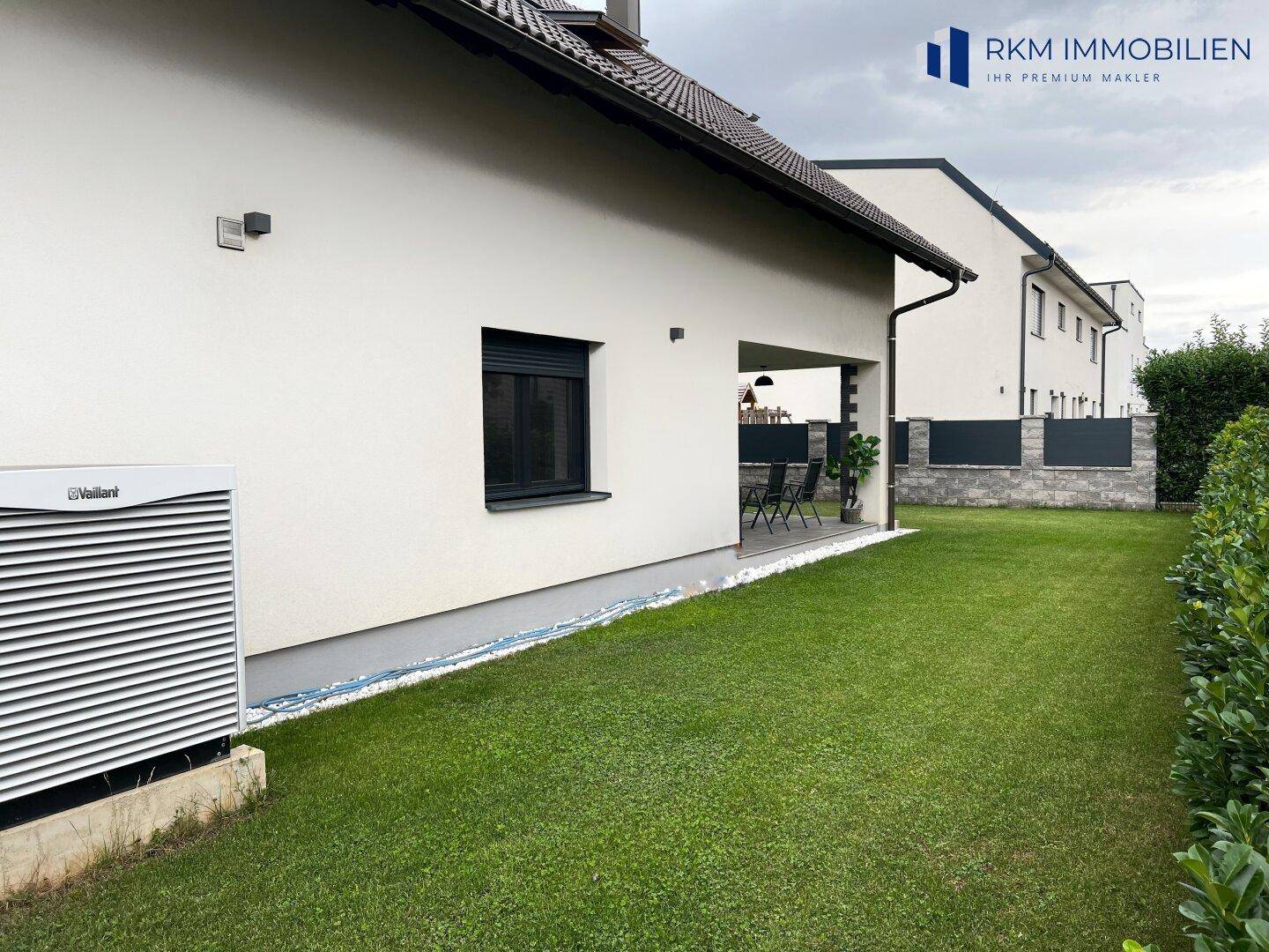 Seitenansicht des Hauses mit einer Wärmepumpe und einem grünen Rasenbereich.