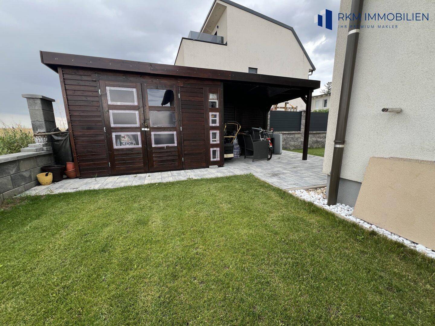 Gartenbereich mit einem Holzschuppen und einem überdachten Carport neben dem Wohnhaus.