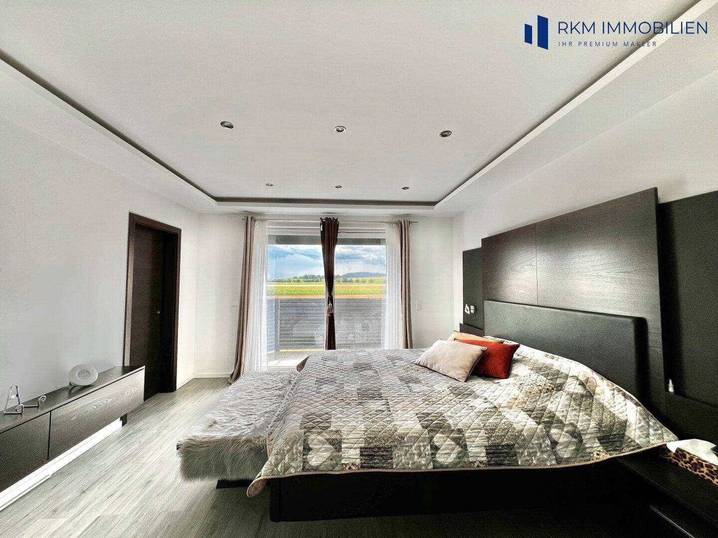 Geräumiges Schlafzimmer mit modernem Bett, dunklen Möbeln und Zugang zum Balkon.