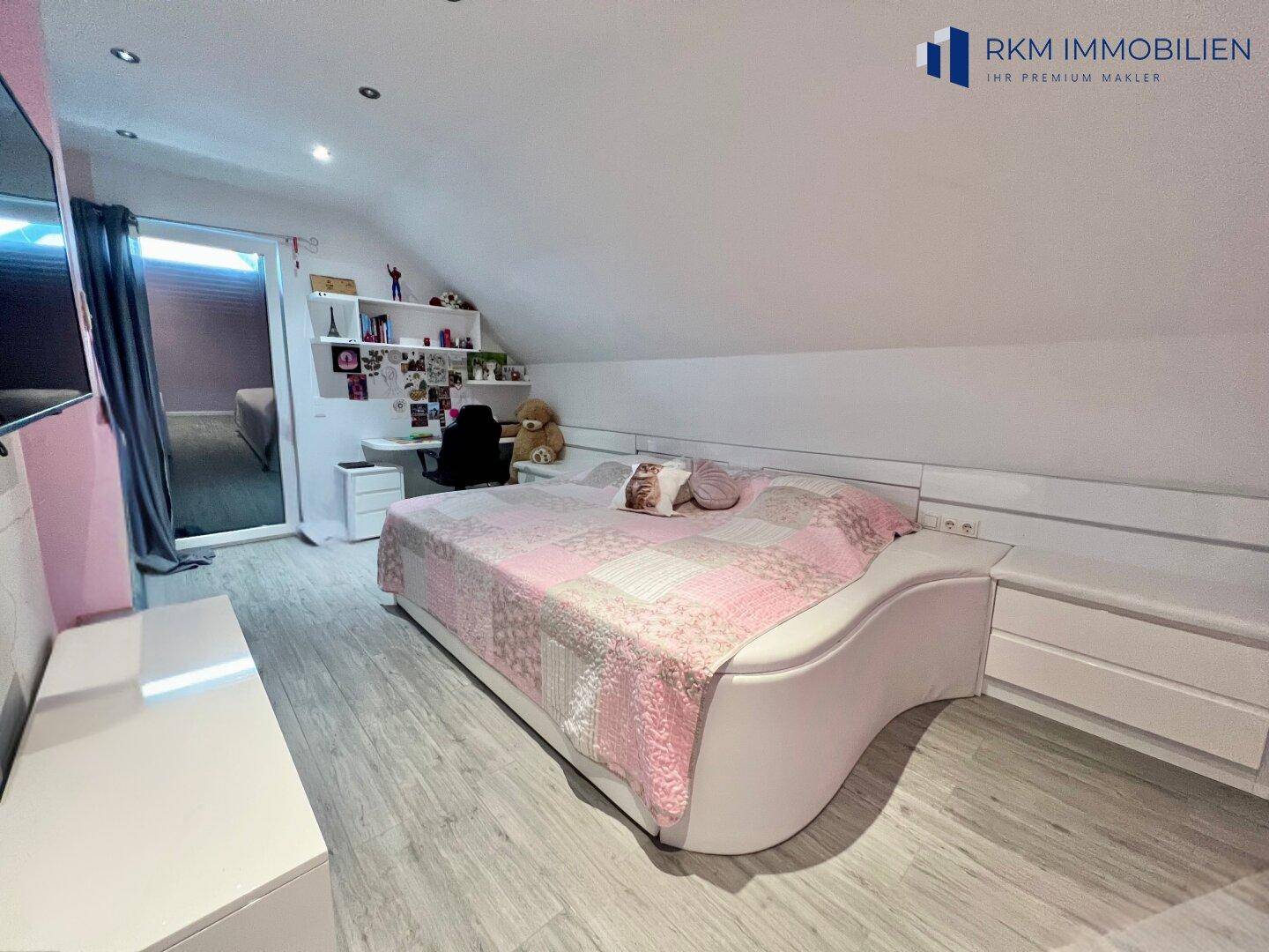 Geräumiges Kinderzimmer mit rosa Akzenten, großem Bett und Schreibtischbereich.