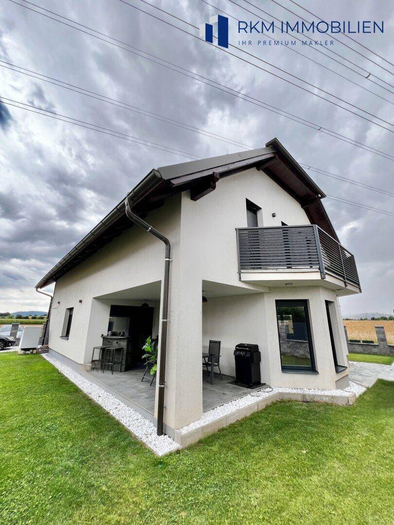 Seitliche Ansicht des modernen Hauses mit einer überdachten Terrasse und gepflegtem Rasen.