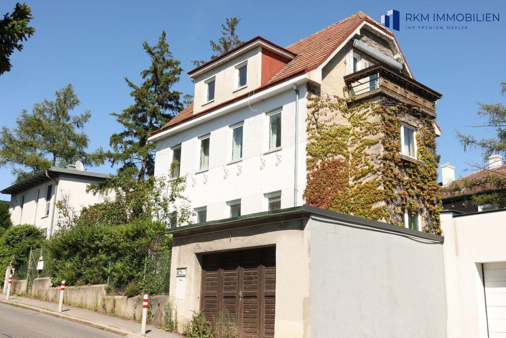 Seitenansicht des Wohnhauses mit Garage, bewachsenen Wänden und rotem Ziegeldach.