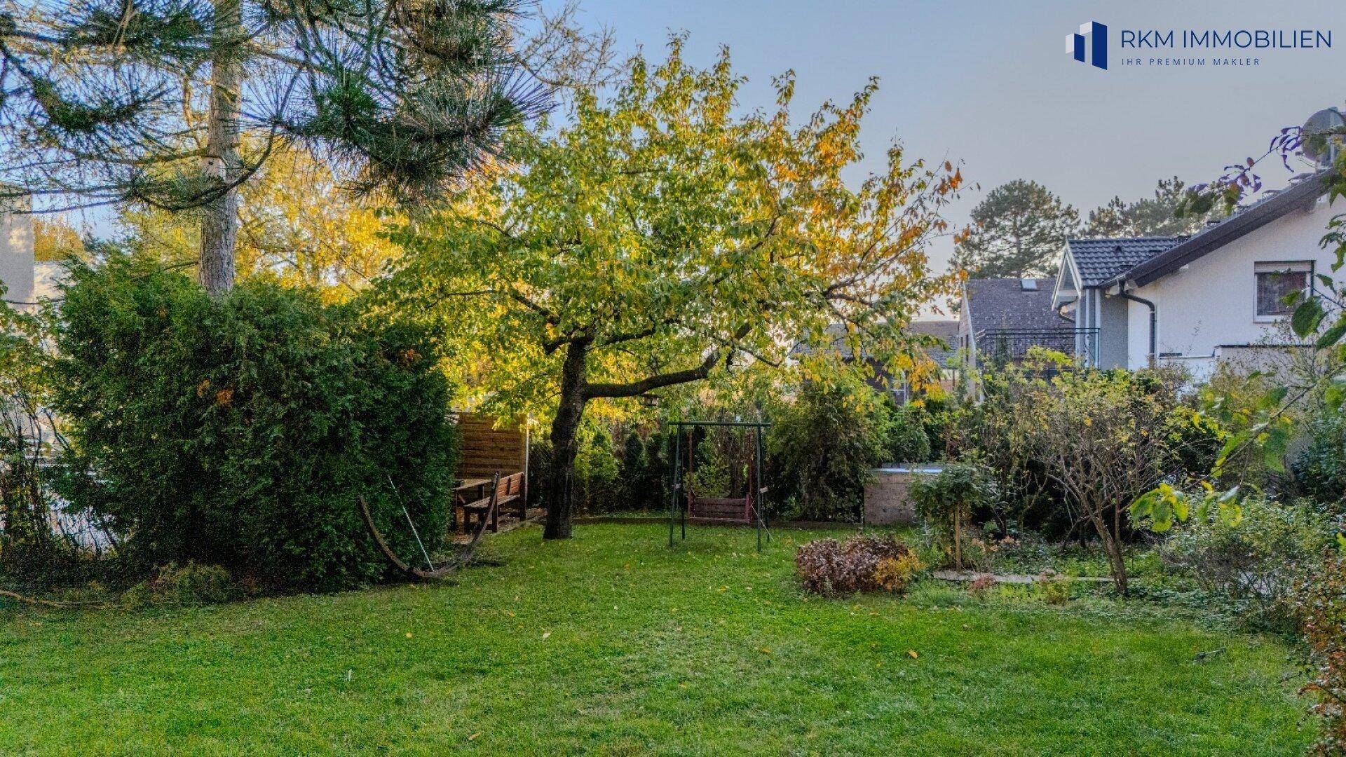 Weitläufiger Garten mit Rasenfläche, Bäumen und einer Schaukel, umgeben von Hecken.