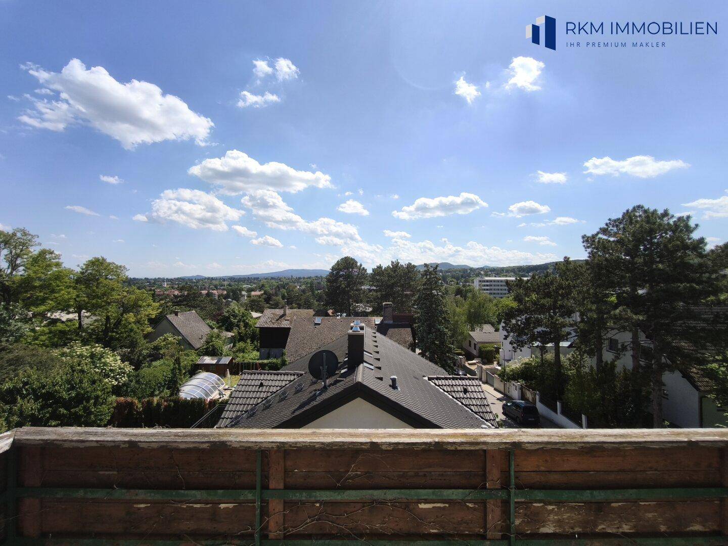 Weitläufiger Ausblick von einem Balkon über die Dächer der Umgebung und grüne Hügel.