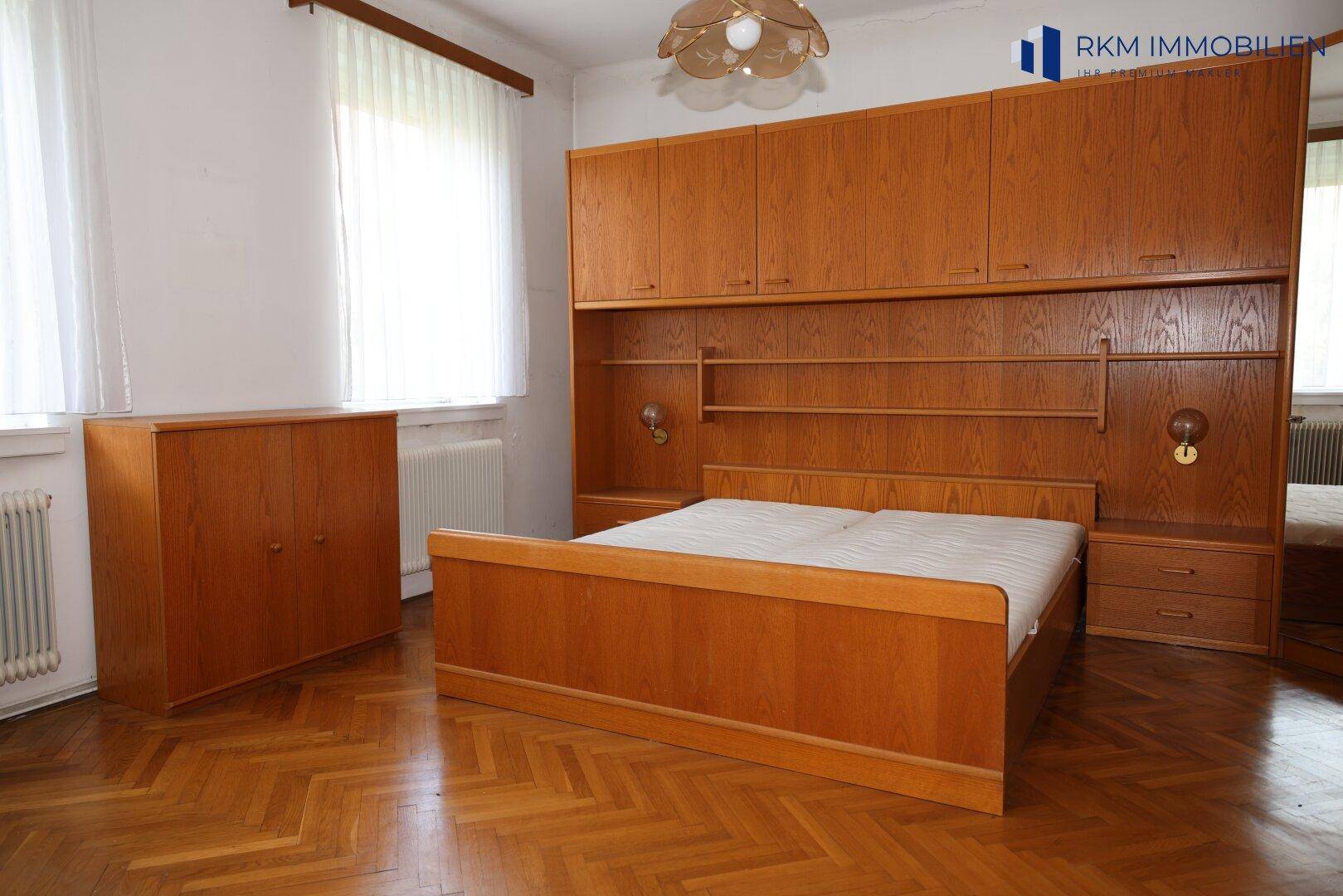 Gemütliches Schlafzimmer mit Holzmöbeln, Parkettboden und viel Tageslicht.