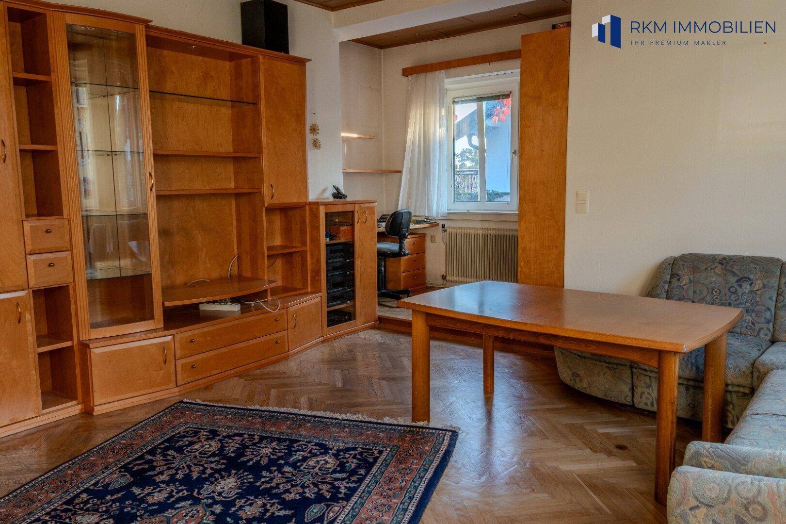 Wohnzimmer mit Holzschrankwand, Esstisch und Parkettboden, hell und geräumig.