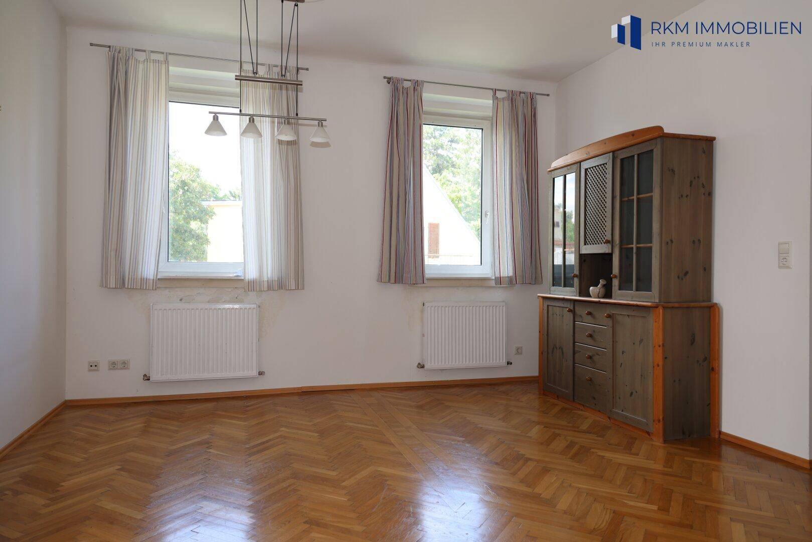 Geräumiges Wohnzimmer mit Fischgrätparkett, großen Fenstern und viel Tageslicht.