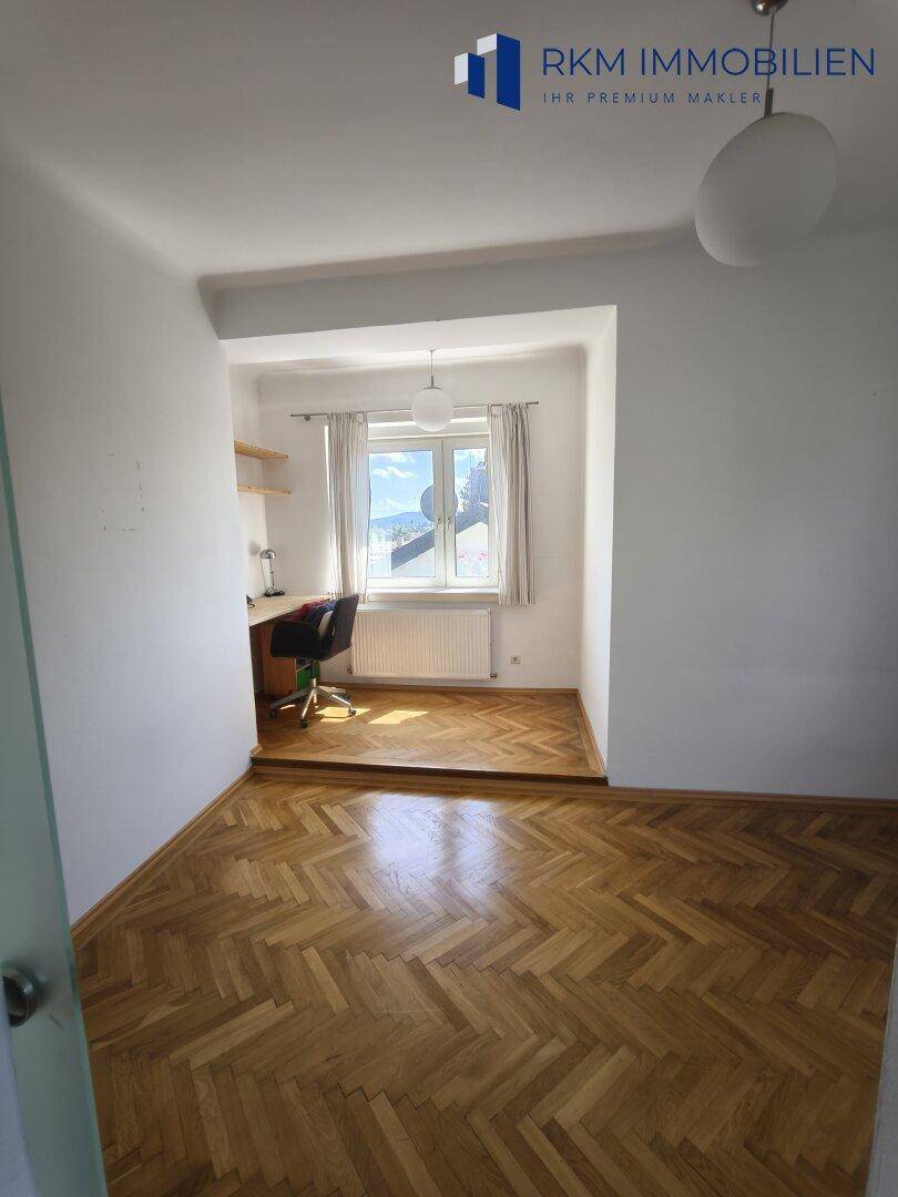 Helles Zimmer mit Fischgrätparkett und einem Arbeitsbereich am Fenster, ideal für Home-Office.