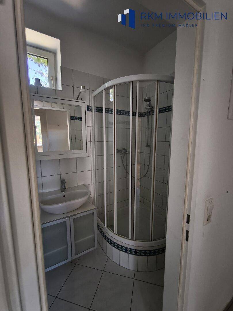 Badezimmer mit Duschkabine, Waschbecken und Fliesenboden, hell und funktional.
