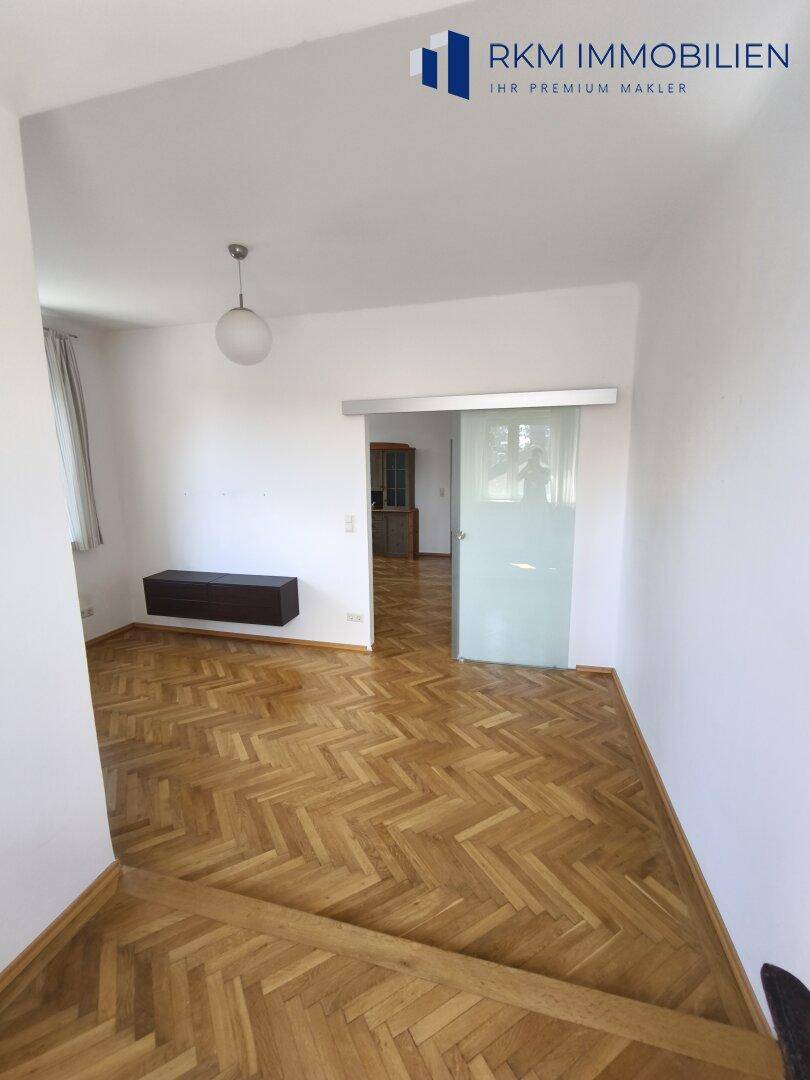 Heller Raum mit Fischgrätparkett und einer Glasschiebetür, die den Übergang zu anderen Bereichen schafft.