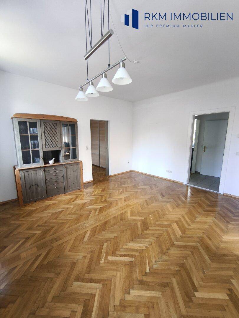 Helles Wohnzimmer mit Fischgrätparkett und Zugang zu weiteren Räumen durch Schiebetüren.