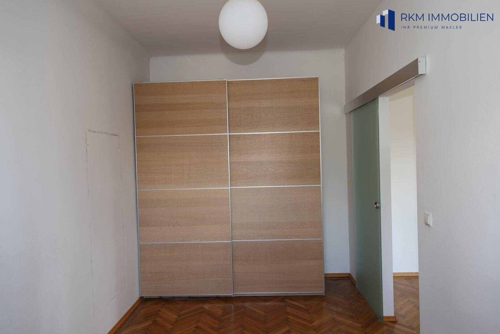 Zimmer mit Fischgrätparkett und einem großen Einbauschrank mit Schiebetüren.