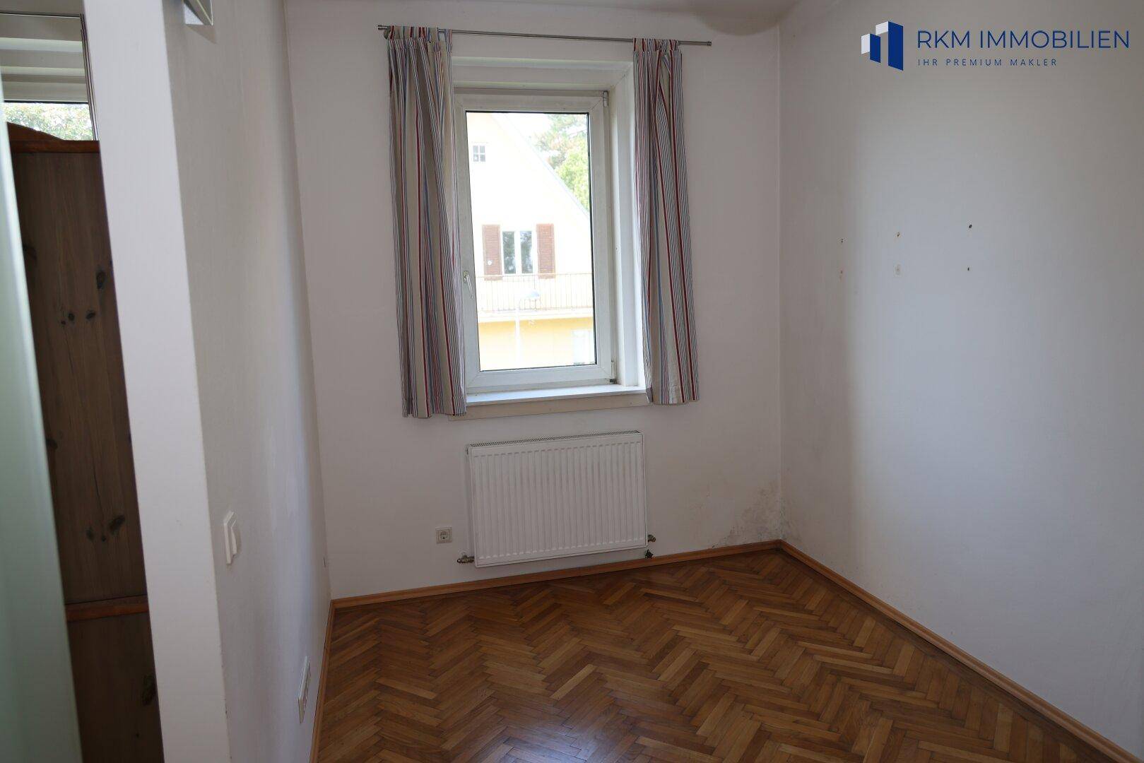 Kleines Zimmer mit Fischgrätparkett und einem Fenster, das viel Tageslicht hereinlässt.