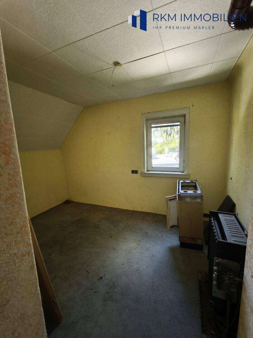Kleiner Raum mit gelben Wänden, Fenster und schräger Decke, ideal als Abstellraum.