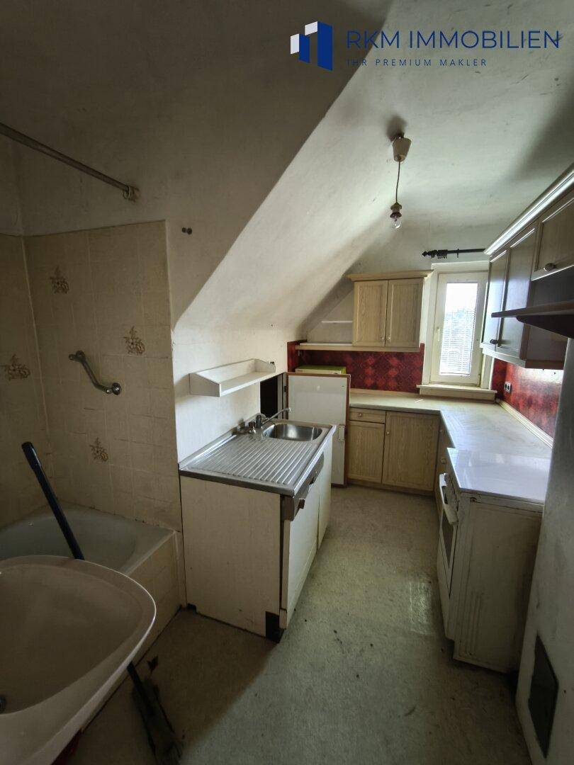 Kleine Küche mit Dachschräge, Einbauschränken und Spülbecken, benötigt Modernisierung.