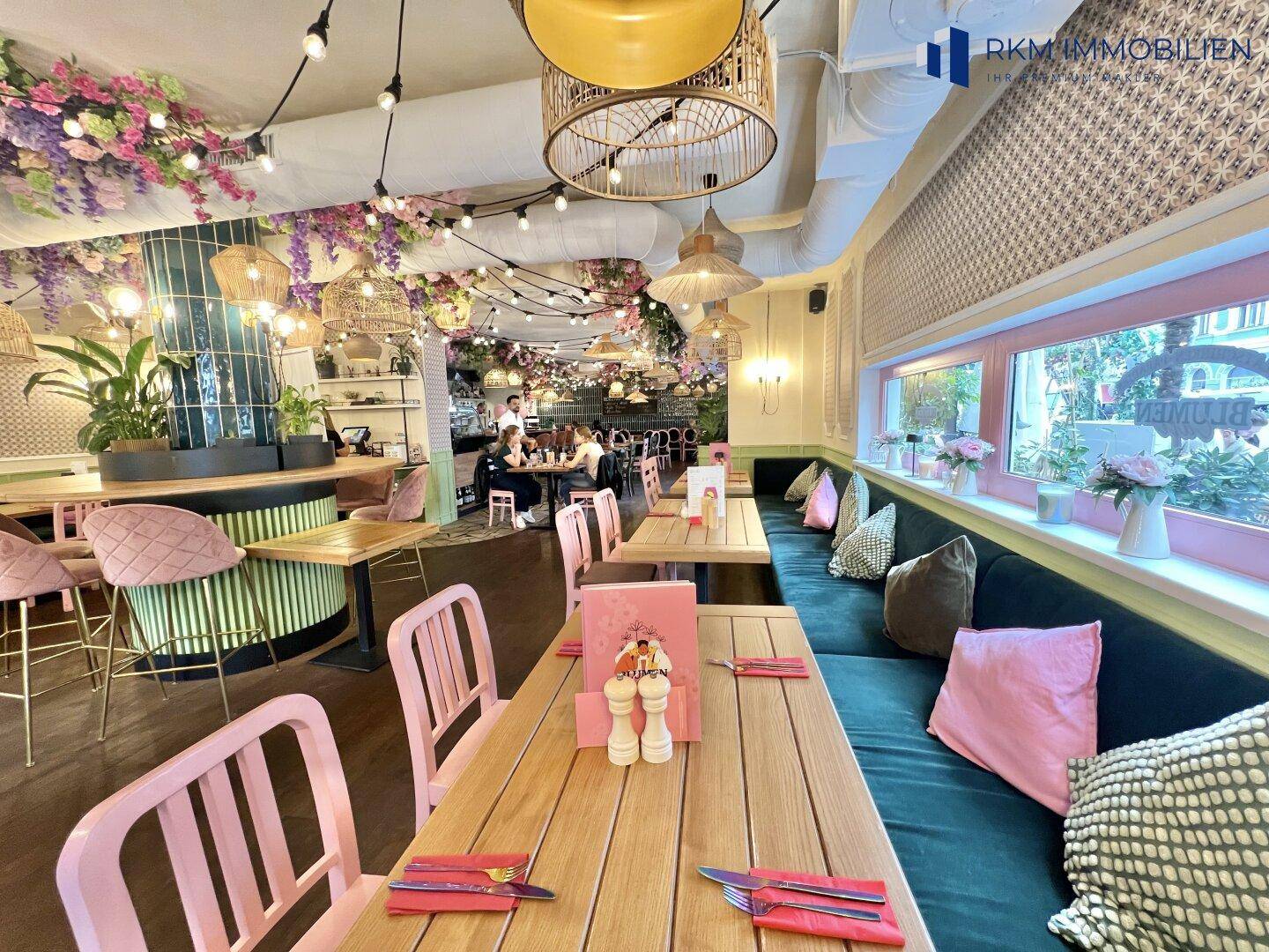 Gemütlicher Restaurantbereich mit langen Sitzbänken, Holztischen und floraler Deckendekoration.