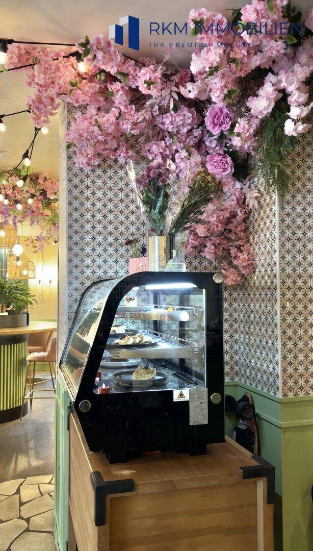 Eine Kuchentheke mit Gebäck in einem stilvoll dekorierten Café mit Blumen an der Wand.